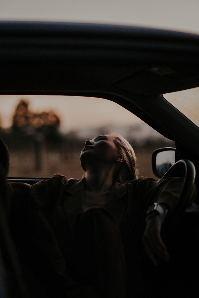 Woman relaxing in car during sunset, peaceful travel moment, scenic outdoor view.