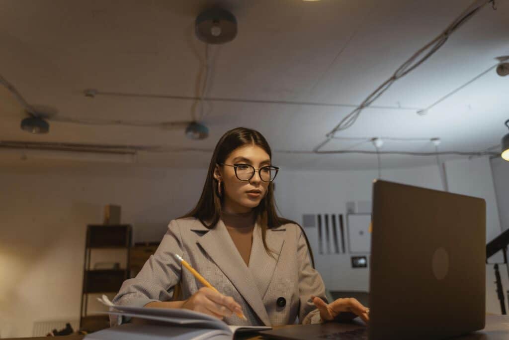 Professional woman working on laptop in a modern office setting with notebooks and pen.
