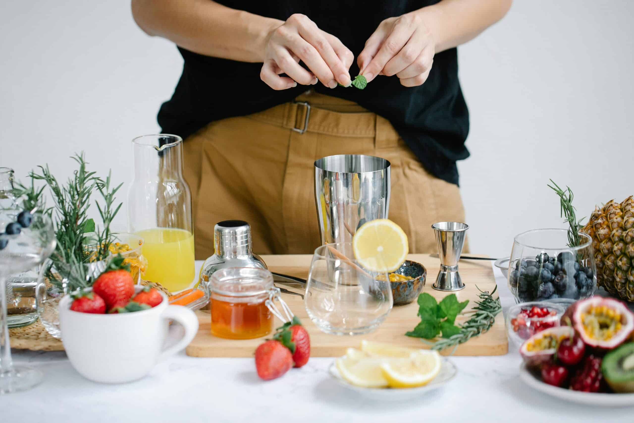 Fresh cocktail preparation with lemons, berries, and herbs on a wooden table.