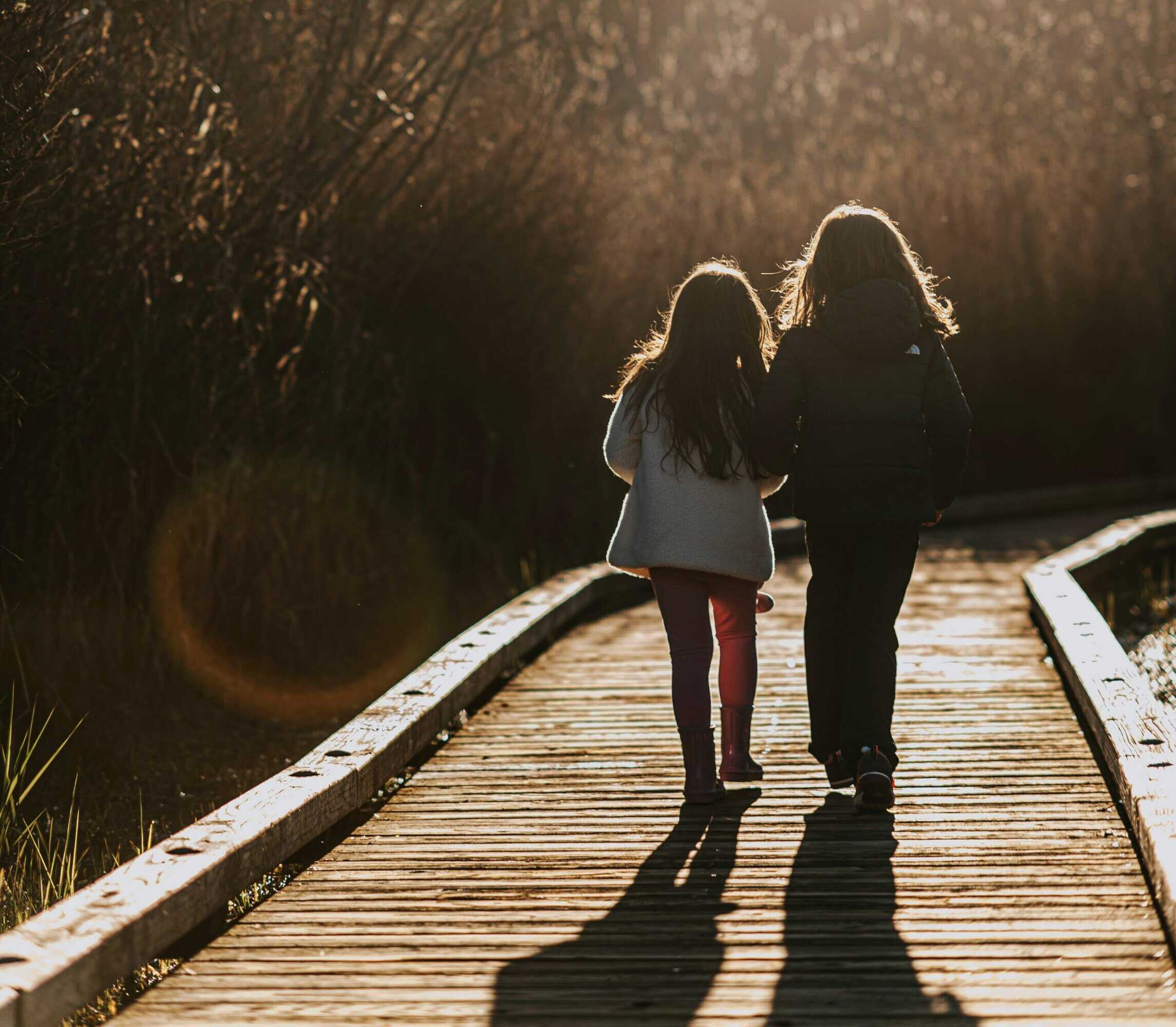 Children walking on a wooden bridge during sunset, enjoying nature and outdoor activities.