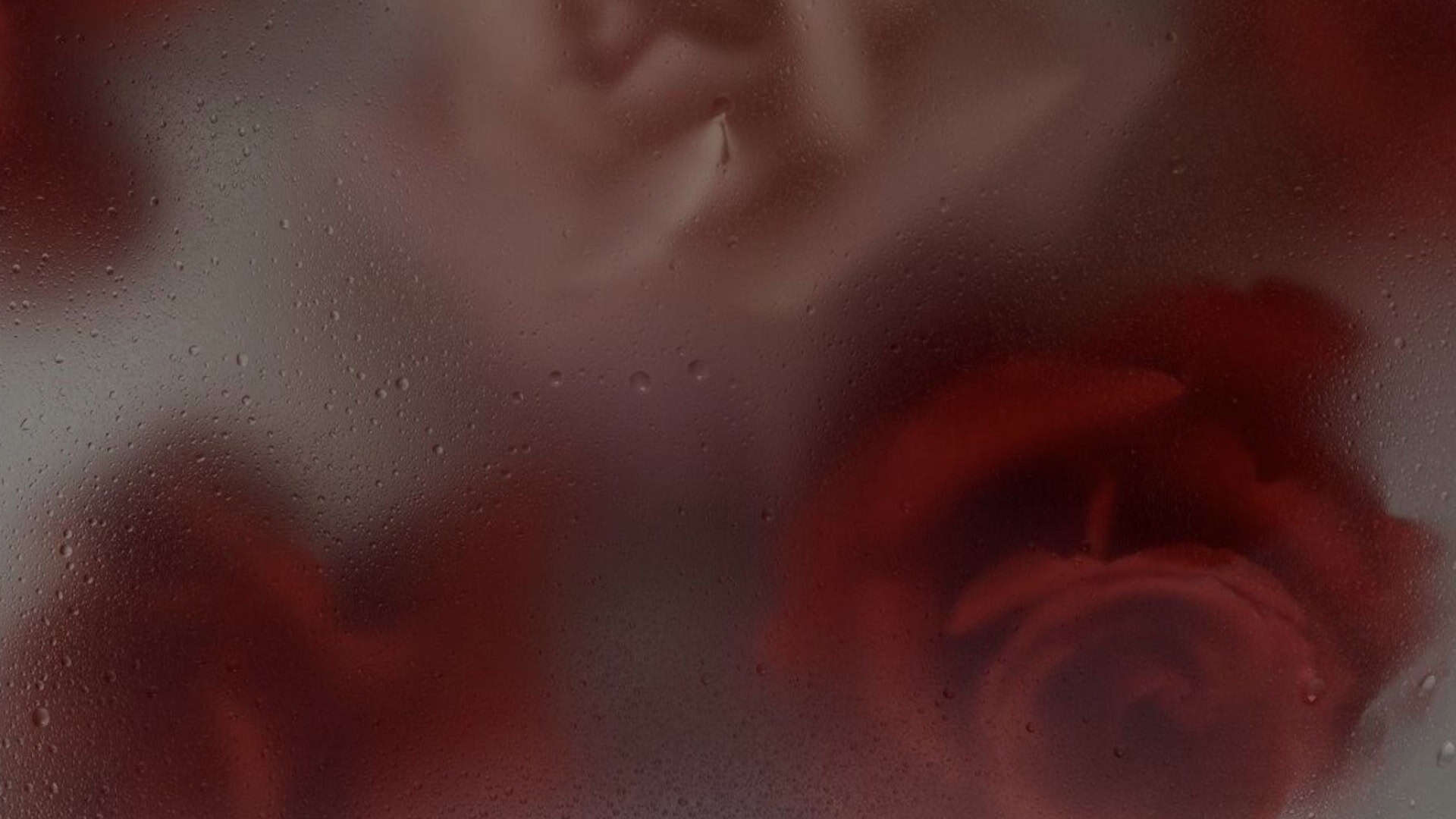 Mysterious close-up of a woman's face behind a foggy glass with water droplets, creating an artistic and alluring effect.