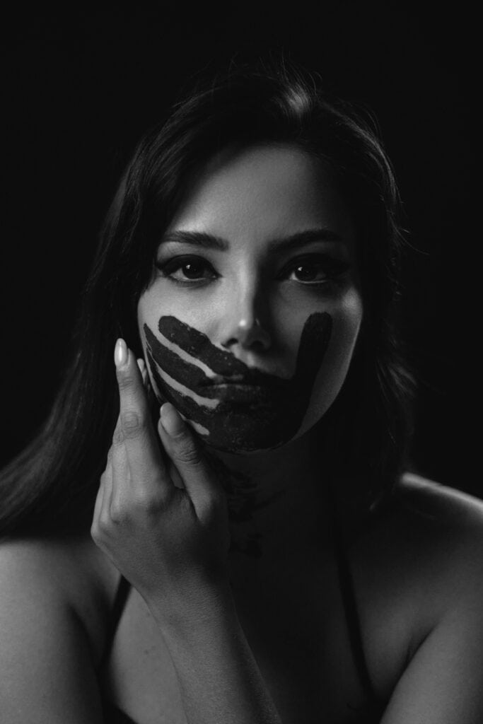 Close-up black and white portrait of a woman with artistic black paint strokes on her face, creating a dramatic and creative look.