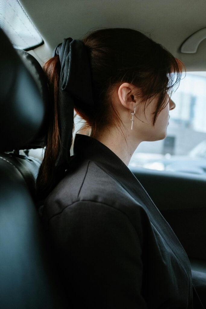 Elegant woman in black jacket with earrings, sitting in car, looking away.