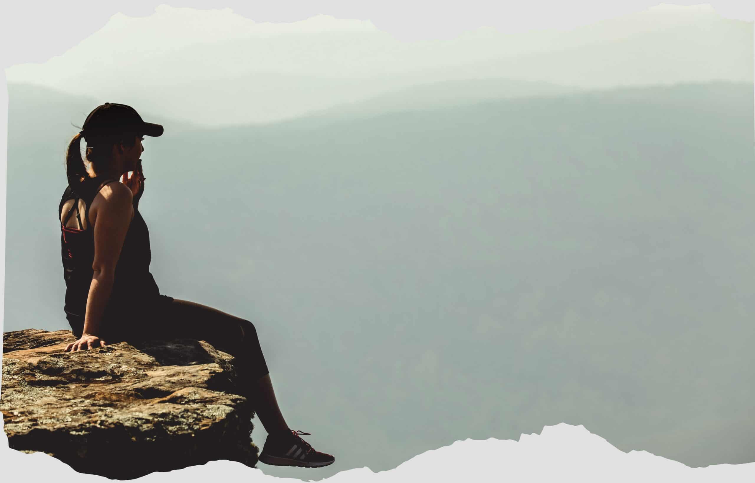 Silent woman sitting on rocky edge overlooking misty mountain landscape, outdoor adventure, travel, nature photography.