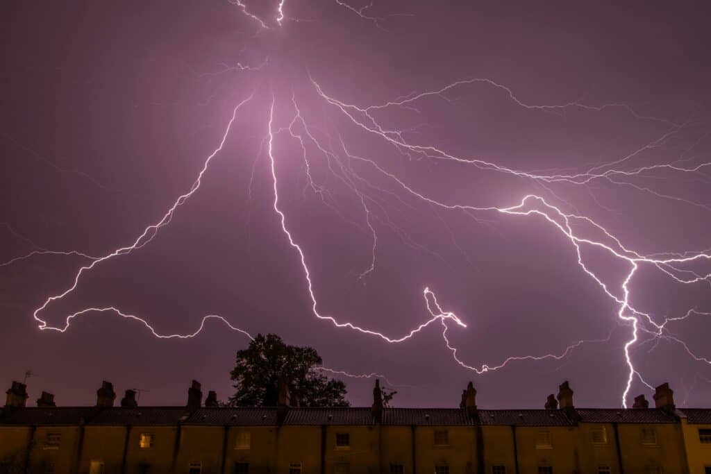 Vivid lightning storm over residential rooftops, showcasing powerful natural electrical activity.