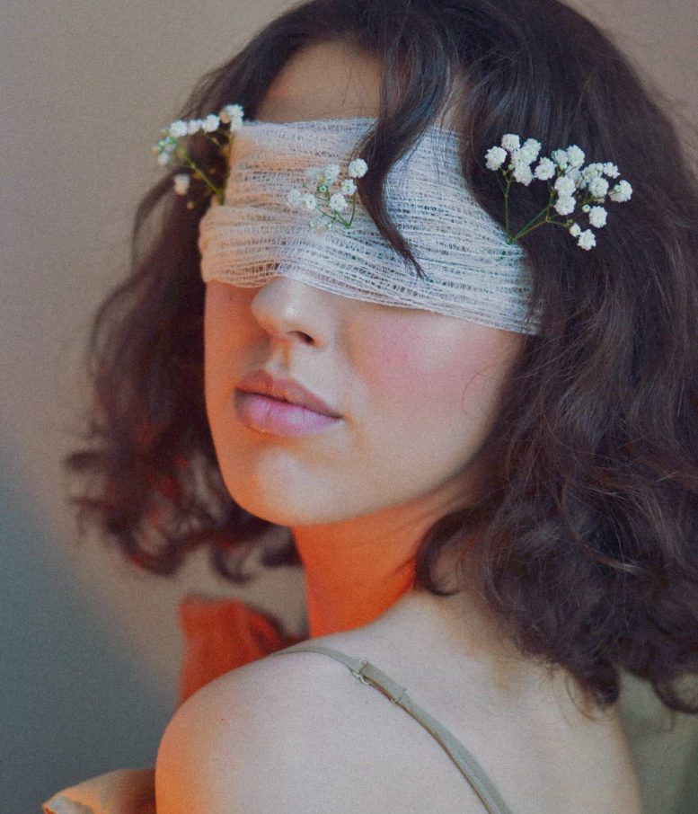 Female model with flowers, blindfolded, in creative and stylish photo.