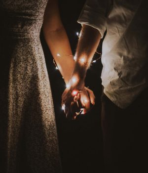 Close-up of couple holding hands wrapped with fairy lights at night.