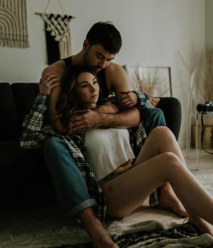 Chic geek couple embracing on sofa in cozy living room.